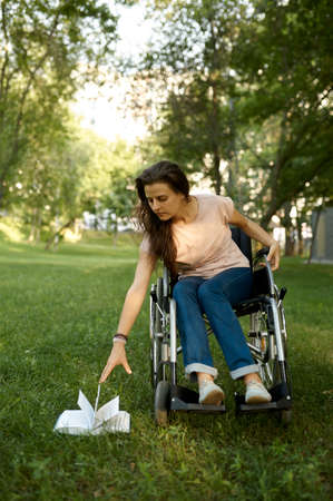Disabled woman in wheelchair tries to pick up bookの写真素材