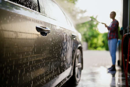 Woman washes off foam from the car, hand auto washの写真素材