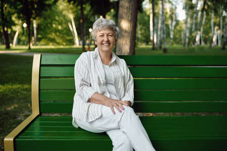 An elderly woman sitting on bench in summer parkの写真素材