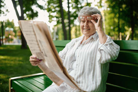 An elderly woman reading newspaper on the benchの写真素材