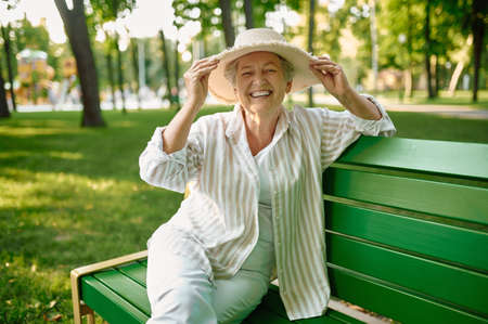 Granny in hat sitting on the bench in summer parkの写真素材