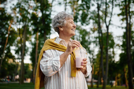 Smiling granny holds milk coctail in summer parkの写真素材
