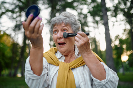 Pretty elderly woman does makeup in summer parkの写真素材