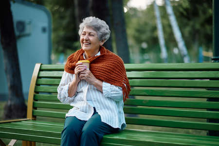 Dranny in scarf drinks hot coffee on the benchの写真素材