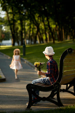 Boy with flowers waiting for a girl on the benchの写真素材