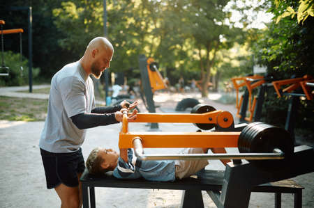 Father helps his son on exercise machineの写真素材