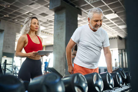 Elderly man takes dumbbells, female trainer, gymの写真素材