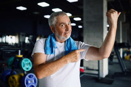 Happy old man shows his muscles in gymの写真素材