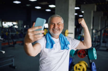 Old man shows his muscles and makes selfie, gymの写真素材