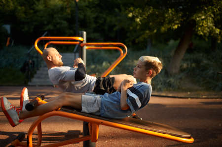 Father and boy doing abs exercise on playgroundの写真素材