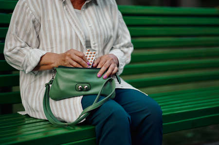 Granny takes pills out of her bag in summer parkの写真素材