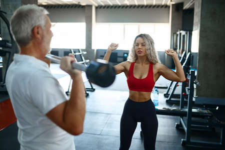 Old man doing exercise with bar, female trainer