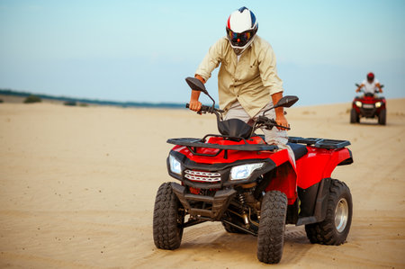 Man poses on atv, downhill riding in desert sandsの写真素材