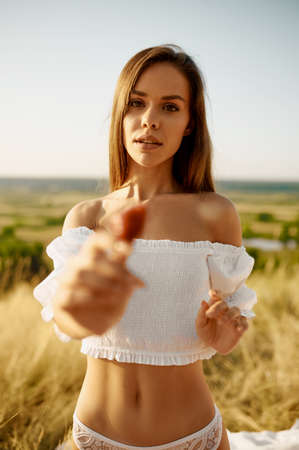 Erotic woman in lingerie shows strawberry in fieldの写真素材