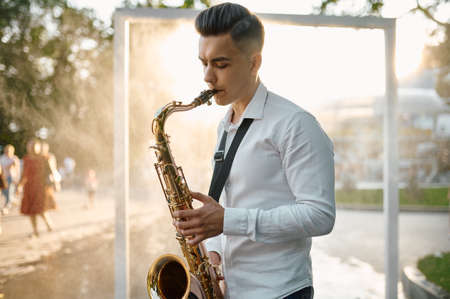 Male saxophonist plays melody on saxophone in parkの写真素材
