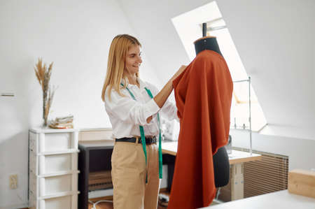 Seamstress tries on dress on mannequin in workshop