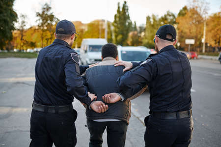 Two male police officers arrest young manの写真素材