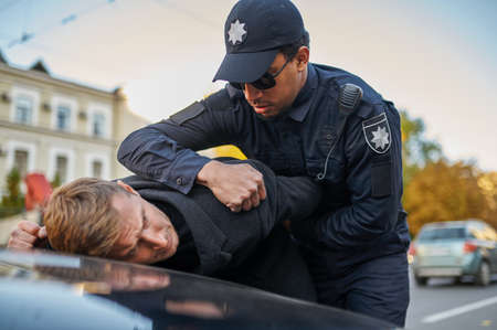 Police officer in sunglasses arrests young man