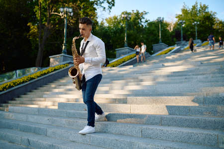 Saxophonist plays the saxophone on stairs in parkの写真素材