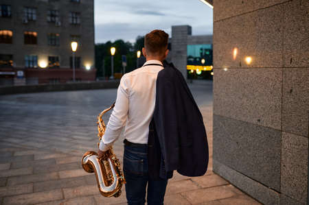 Male saxophonist with sax on street in the eveningの写真素材