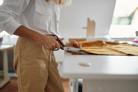 Seamstress with scissors cuts cloth in workshopの写真素材