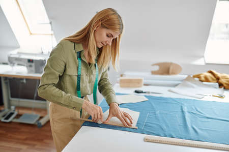 Seamstress with scissors cuts cloth in workshopの写真素材