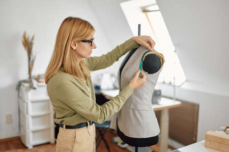 Dressmaker measures dress on mannequin in workshop