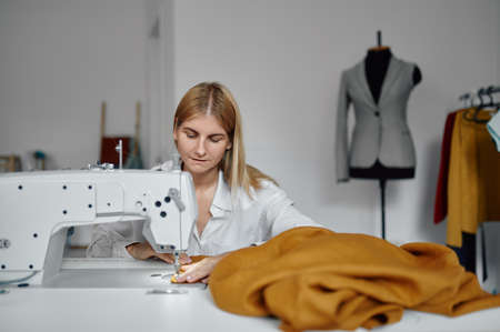Dressmaker sews cloth on sewing machine, workshop