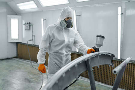 Painter in protective mask painting automobile part