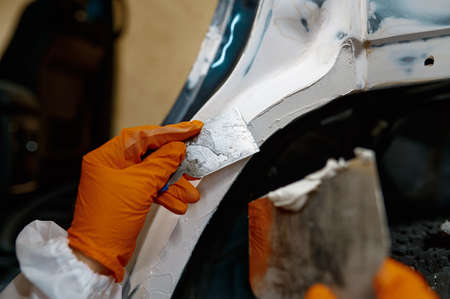 Mechanic puttying plastering car body in garageの写真素材