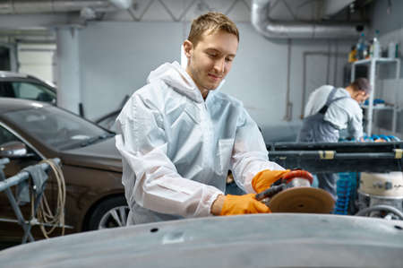 Serviceman polishing car body part in workshopの写真素材