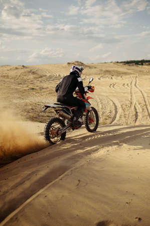 Professional motocross rider driving on sand dune