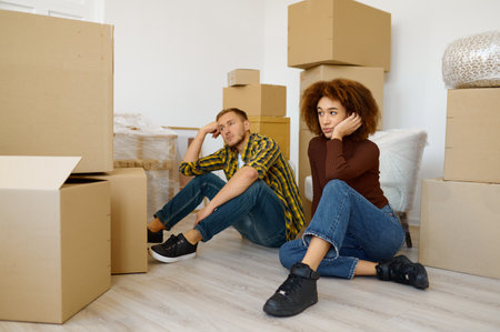 Tired multiracial couple sitting among cardboard boxesの写真素材