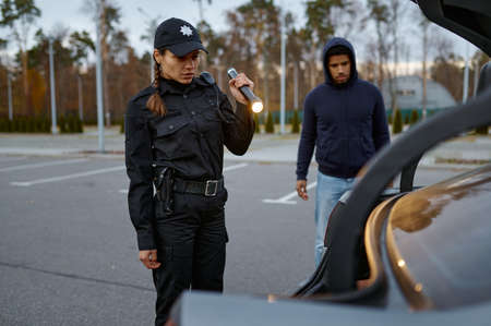 Woman police officer inspecting car with flashlightの写真素材