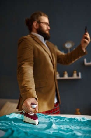 Businessman having phone video chat ironing clothes
