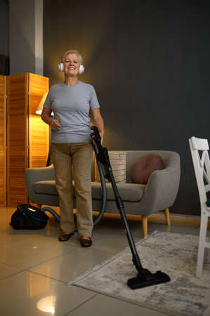 Old woman listening music cleaning floor carpetの写真素材