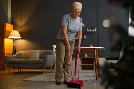 Aged mature woman sweeping floor at homeの写真素材