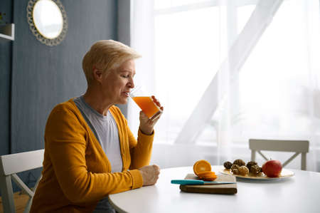 Smiling grey-haired woman holding glass with juiceの写真素材