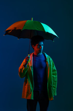 Man in raincoat under umbrella over dark studio backgroundの写真素材