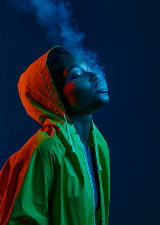 Hipster woman in raincoat blowing smoke from mouthの写真素材