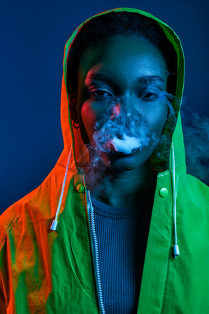 Hipster woman in raincoat blowing smoke from mouthの写真素材