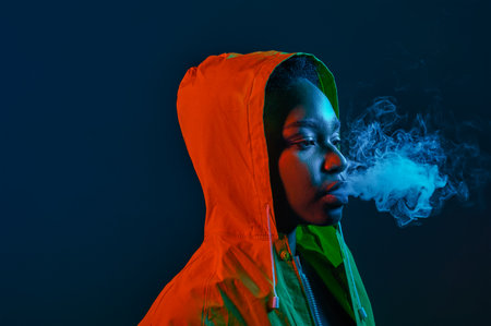 Hipster woman in raincoat blowing smoke from mouthの写真素材