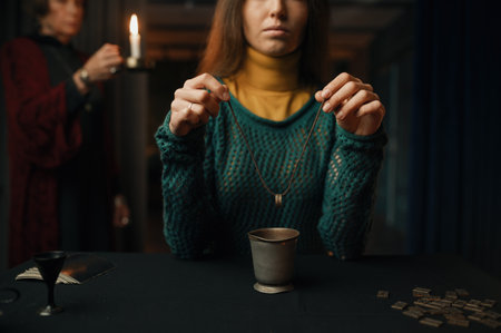 Woman making divination with ring under mature professional gypsy controlの写真素材
