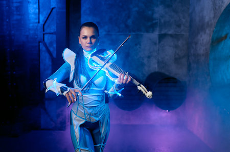 Young woman playing violin solo on stage illuminated with neon lightの写真素材