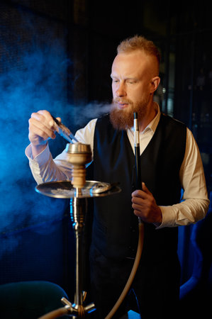 Stylish bearded man mixing tobacco in hookah and smokingの写真素材