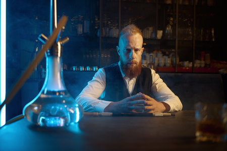 Portrait of lonely bearded man smoking hookah and drinking brandyの写真素材