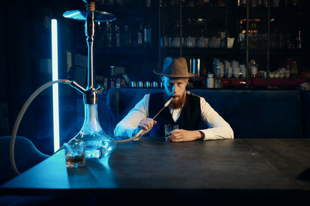 Portrait of stylish bearded man with hat smoking hookahの写真素材