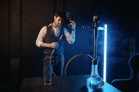 Portrait of stylish bearded man with hat smoking hookahの写真素材