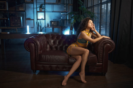 Sensual woman in sexy lingerie with yellow laces sitting on leather sofaの写真素材