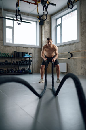 Muscular shirtless man working out with heavy ropesの写真素材